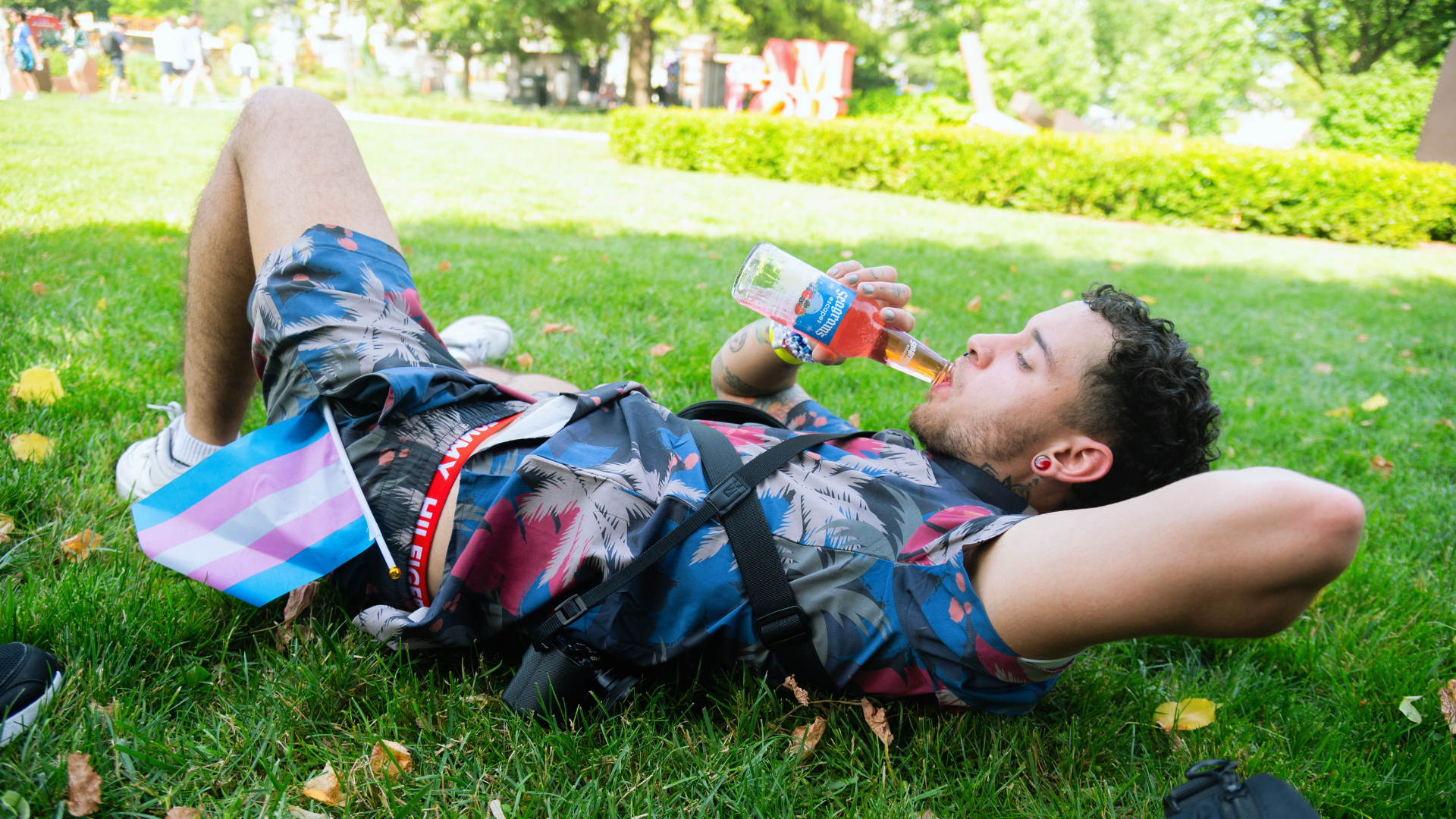 Trans man relaxing on the grass with a Seagram's drink at DC Pride 2024, trans flag visible.